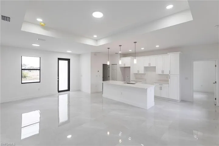 Kitchen with a kitchen island with sink, white cabinets, decorative light fixtures, sink, and a tray ceiling