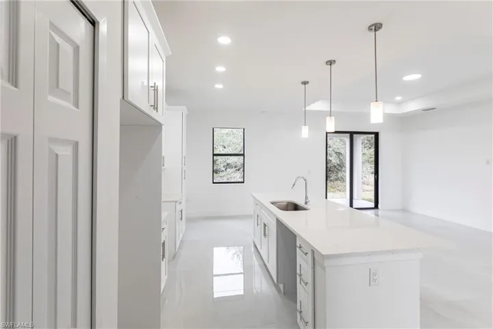 Kitchen featuring light stone countertops, white cabinetry, sink, hanging light fixtures, and a kitchen island with sink