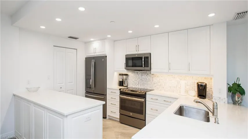 Kitchen with appliances with stainless steel finishes, white cabinetry, sink, decorative backsplash, and kitchen peninsula