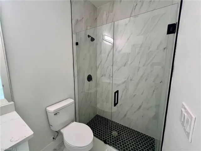 Bathroom with toilet, vanity, and a shower with frameless glass  shower door