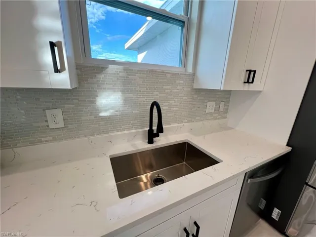 Kitchen featuring white cabinets, decorative glass tile backsplash, light QUARTZ counters, and sink