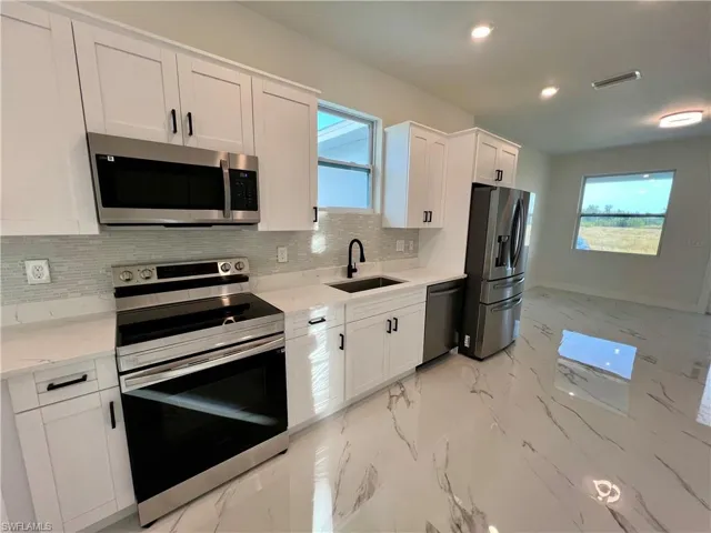Kitchen with appliances with stainless steel finishes, light QUARTZ counters, a healthy amount of sunlight, sink, and white cabinetry