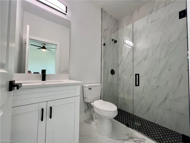 Primary Bathroom featuring walk in shower with frameless glass doors, vanity, and toilet
