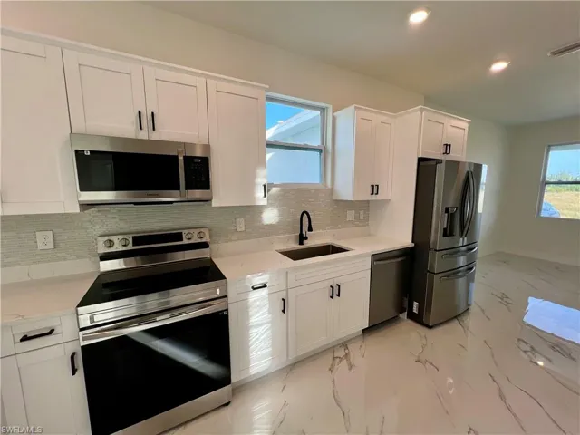 Kitchen featuring decorative backsplash, appliances with stainless steel finishes, QUARTZ counters, sink, and white cabinetry