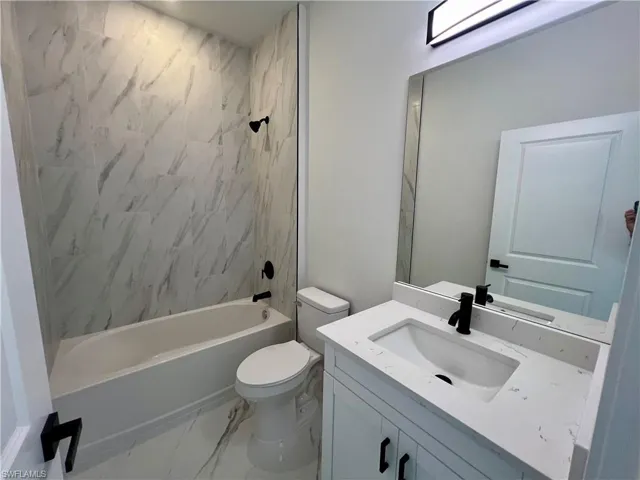 Full bathroom featuring toilet, vanity, and tiled shower / bath with QUARTZ tops.