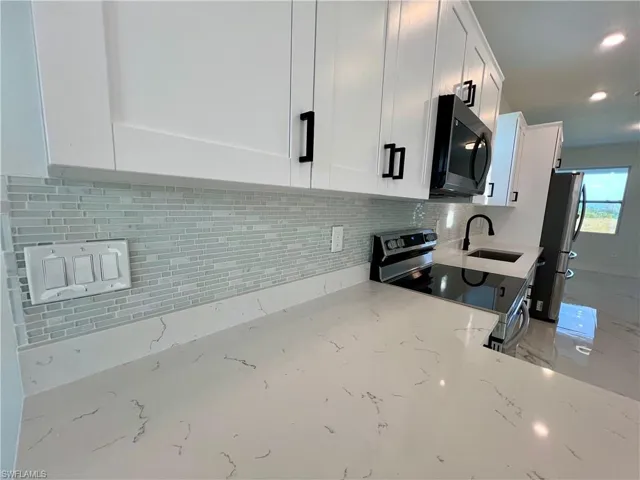 Kitchen with white cabinetry, sink, glass tile backsplash, light QUARTZ countertops, and stainless steel appliances