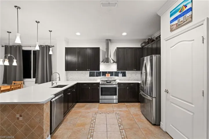 Kitchen featuring stainless steel appliances, decorative backsplash, wall chimney exhaust hood, sink, and light tile patterned floors