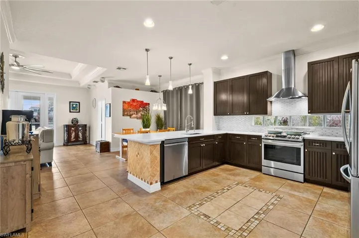 Kitchen featuring crown molding, kitchen peninsula, wall chimney exhaust hood, appliances with stainless steel finishes, and a raised ceiling