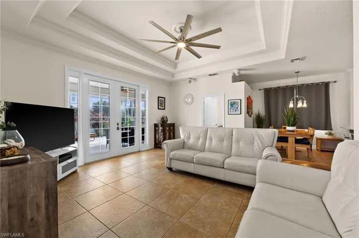 Living room featuring ceiling fan with notable chandelier, french doors, a raised ceiling, and crown molding