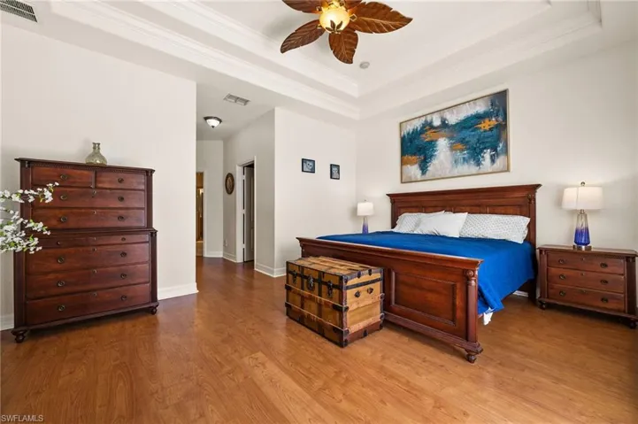 Another angle showing the beautiful wood-style flooring, a raised ceiling, crown molding, and ceiling fan