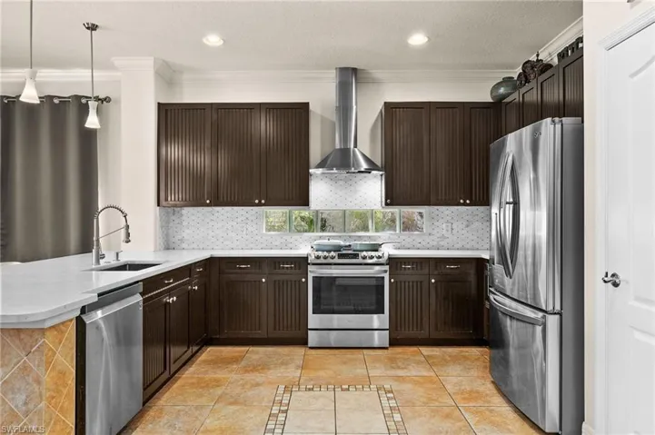 Kitchen featuring appliances with stainless steel finishes, sink, kitchen peninsula, pendant lighting, and wall chimney exhaust hood