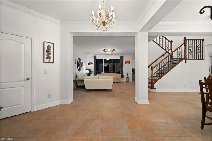 Foyer entrance with light tile patterned flooring, ornamental molding, and an inviting chandelier