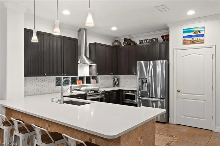 Kitchen featuring stainless steel appliances, wall chimney exhaust hood, a kitchen bar, kitchen peninsula, and backsplash