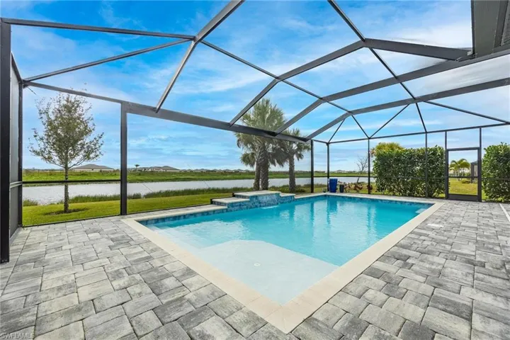 View of pool with glass enclosure, a patio area, and a water view