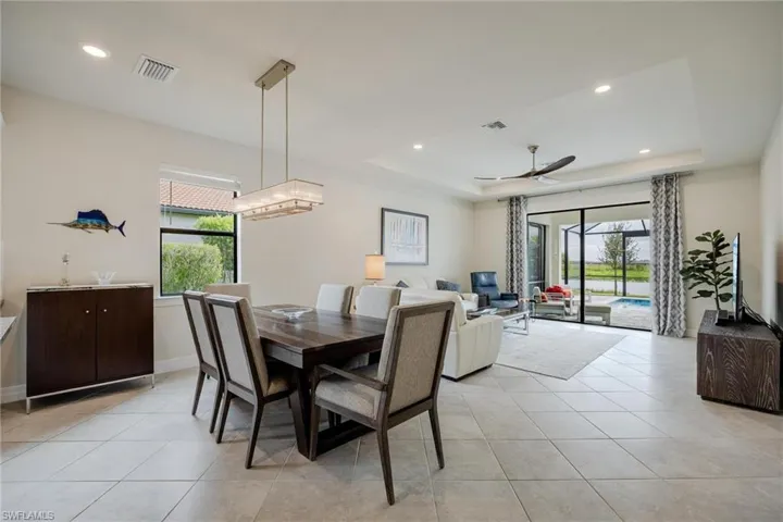 Tiled dining area with ceiling fan with notable chandelier and a tray ceiling