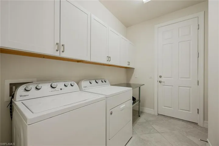 Laundry room with independent washer and dryer, light tile patterned flooring, and cabinets
