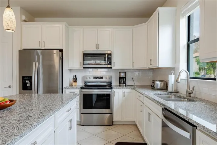 Kitchen with sink, white cabinets, hanging light fixtures, and appliances with stainless steel finishes