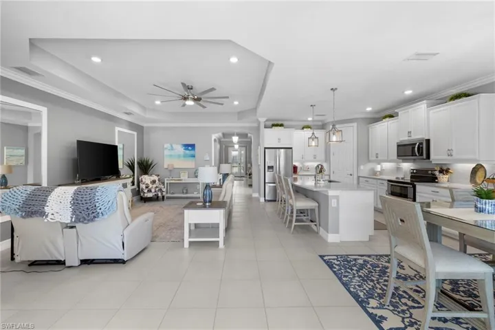 Living room with a tray ceiling, ceiling fan, light tile patterned floors, and ornamental molding