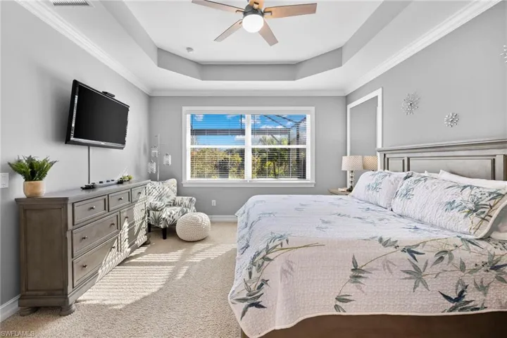 Bedroom featuring ceiling fan, a raised ceiling, carpet floors, and ornamental molding