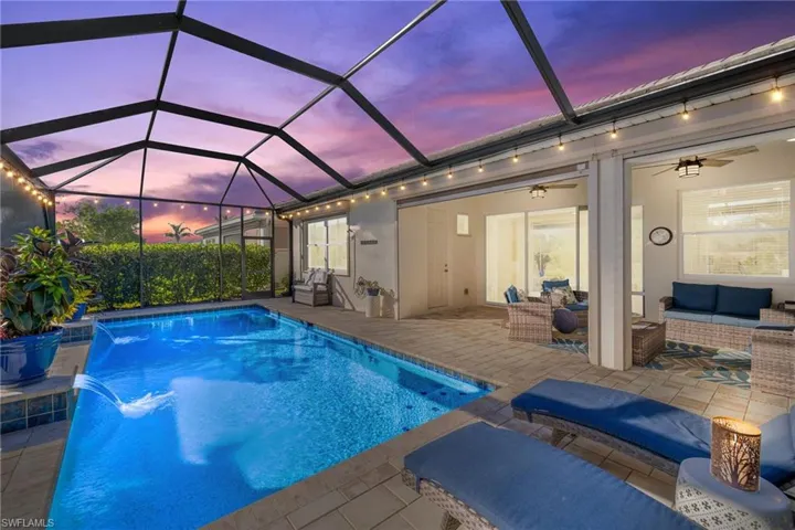 Pool at dusk with outdoor lounge area, pool water feature, ceiling fan, glass enclosure, and a patio area