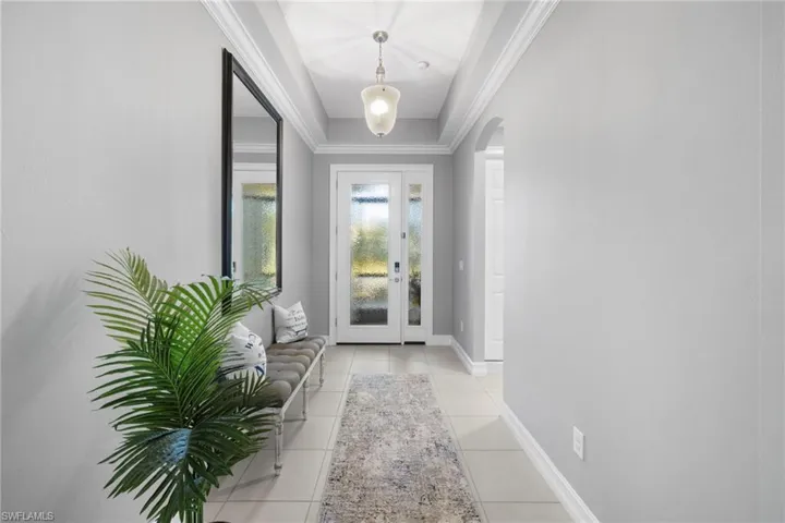 Entryway with light tile patterned flooring, ornamental molding, and a tray ceiling