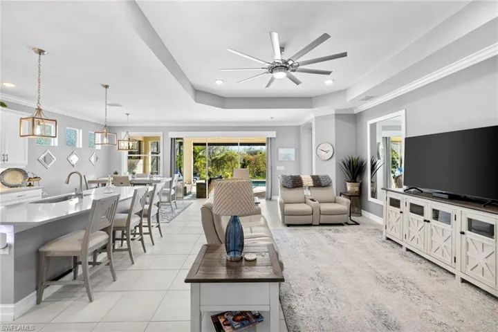 Living room with ceiling fan, sink, a tray ceiling, light tile patterned floors, and ornamental molding