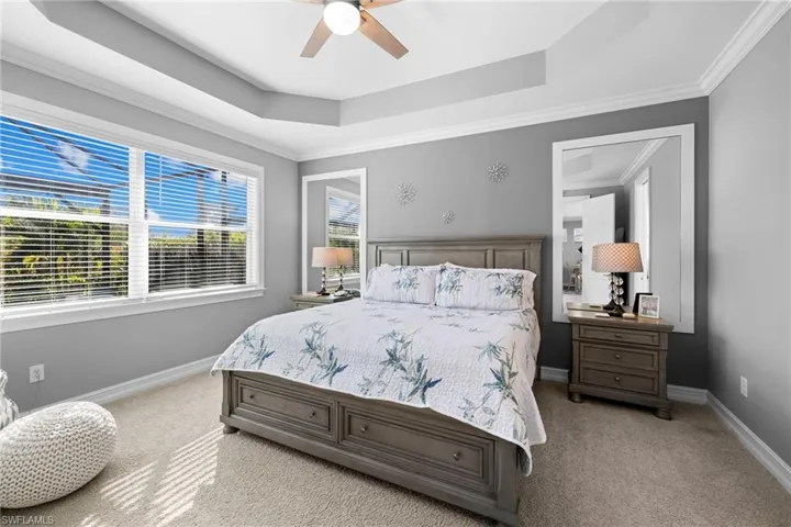 Carpeted bedroom with a tray ceiling, ceiling fan, and ornamental molding