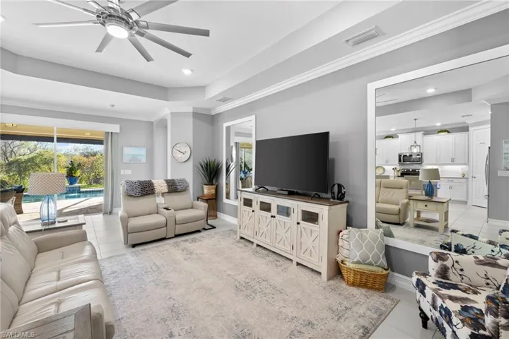 Tiled living room with ceiling fan, ornamental molding, and a tray ceiling