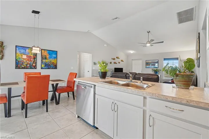 Kitchen featuring light countertops, white cabinetry, stainless steel dishwasher, hanging light fixtures, and vaulted ceiling