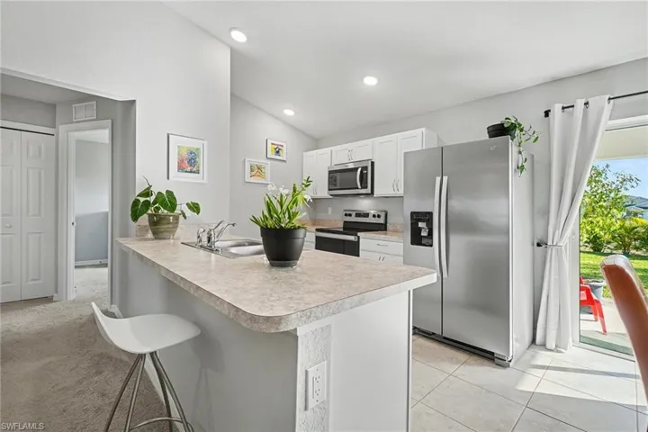 Kitchen with stainless steel appliances, a breakfast bar area, white cabinets, light countertops, and vaulted ceiling