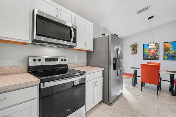 Kitchen featuring stainless steel appliances, light countertops, white cabinetry, decorative light fixtures, and lofted ceiling
