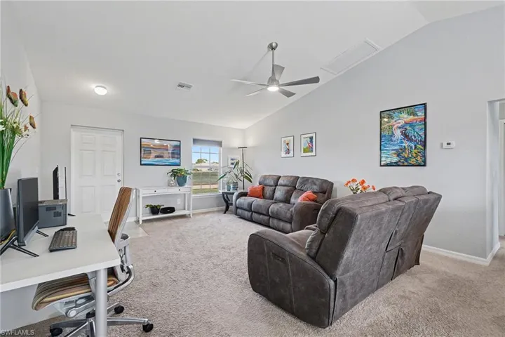 Living area featuring a desk, vaulted ceiling, light carpet, and a ceiling fan