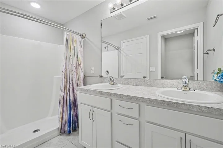 Bathroom with a shower stall, double vanity, and light tile patterned flooring