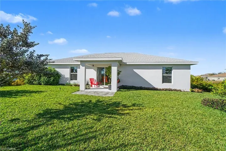 Back of property featuring stucco siding, a lawn, a patio area, and a shingled roof