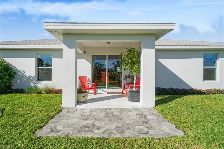Doorway to property featuring roof with shingles, a lawn, and stucco siding