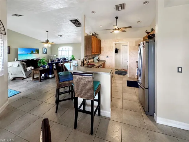 Kitchen with freestanding refrigerator, a ceiling fan, open floor plan, a breakfast bar, and vaulted ceiling