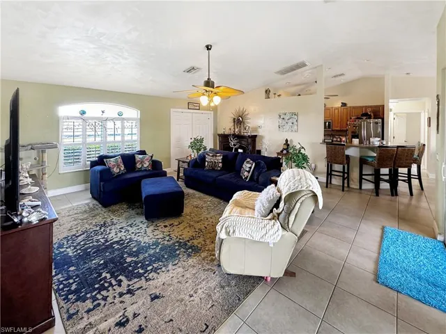 Living room with light tile patterned flooring, ceiling fan, and vaulted ceiling
