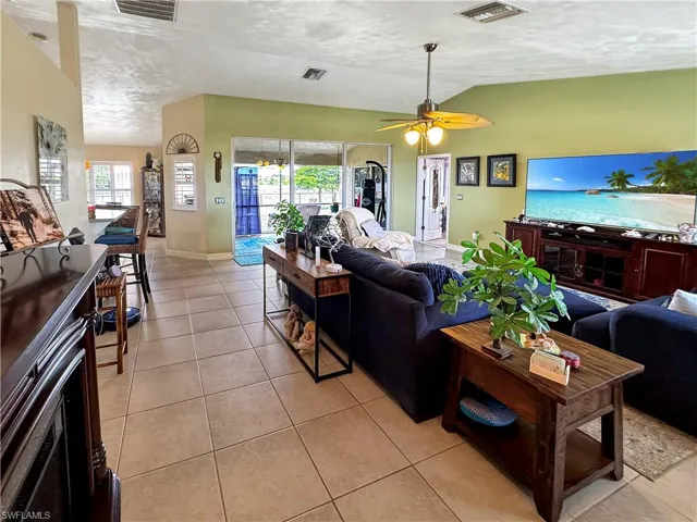 Living room with lofted ceiling, light tile patterned flooring, plenty of natural light, ceiling fan, and a textured ceiling