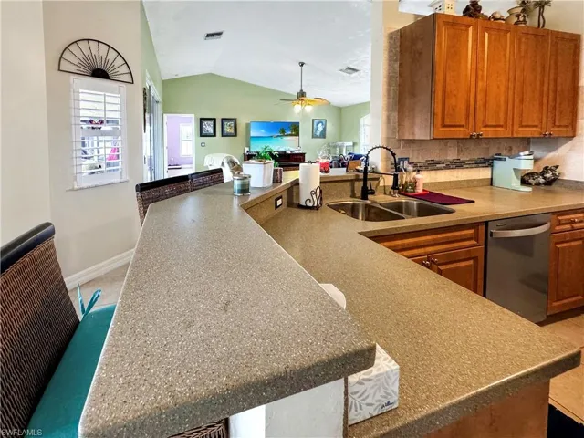 Kitchen featuring stainless steel dishwasher, ceiling fan, brown cabinets, lofted ceiling, and open floor plan