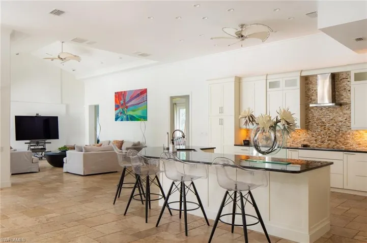Kitchen featuring white cabinets, wall chimney exhaust hood, a spacious island, and a breakfast bar