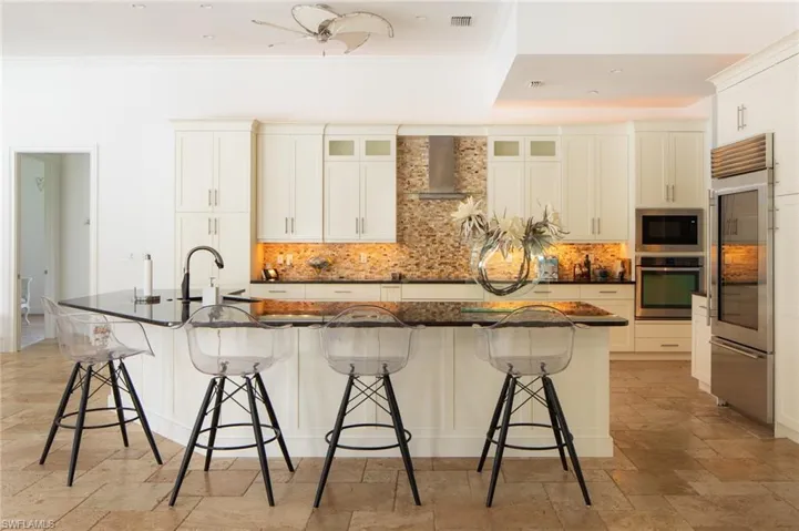 Kitchen featuring built in appliances, a breakfast bar area, tasteful backsplash, wall chimney range hood, and a spacious island