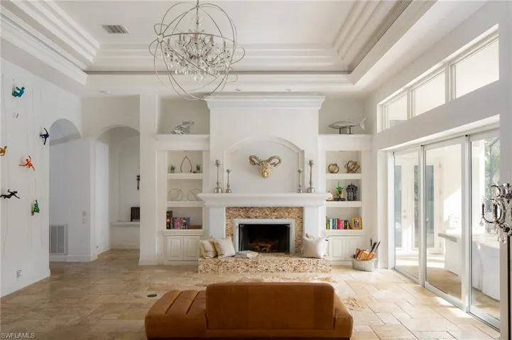 Living room with a tray ceiling, an inviting chandelier, built in shelves, and ornamental molding