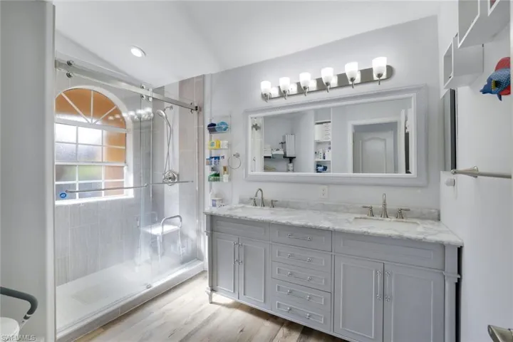 Bathroom with vanity, hardwood / wood-style flooring, a shower with shower door, and lofted ceiling