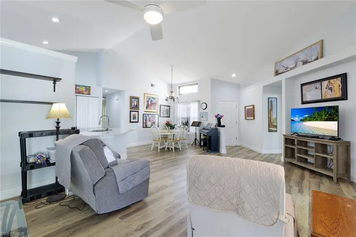 Living room with ceiling fan with notable chandelier, light wood-type flooring, lofted ceiling, and sink
