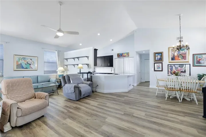 Living room featuring sink, high vaulted ceiling, ceiling fan with notable chandelier, and light wood-type flooring