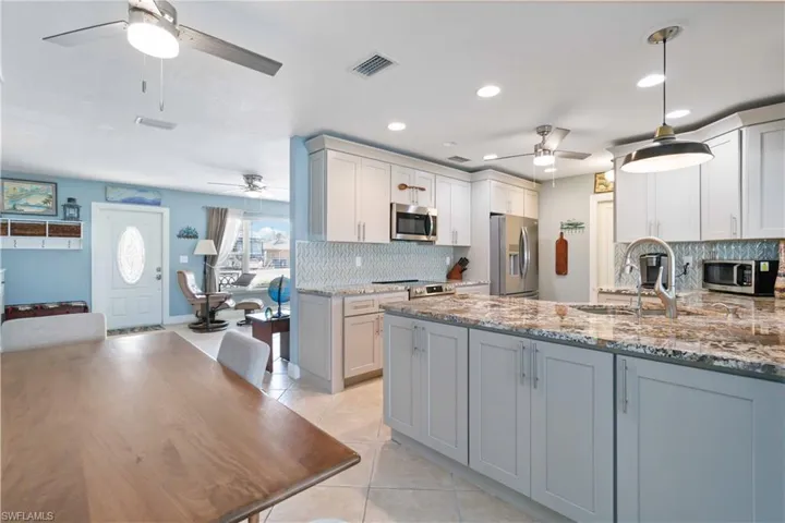 Kitchen with light stone counters, light tile patterned floors, stainless steel appliances, visible vents, and a sink