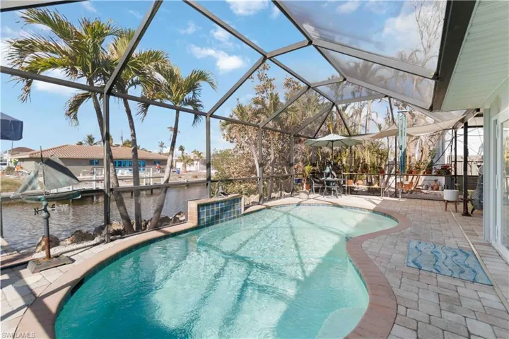 Outdoor pool with glass enclosure, a water view, and a patio