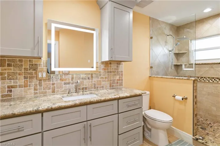 Bathroom with recessed lighting, backsplash, toilet, vanity, and a walk in shower