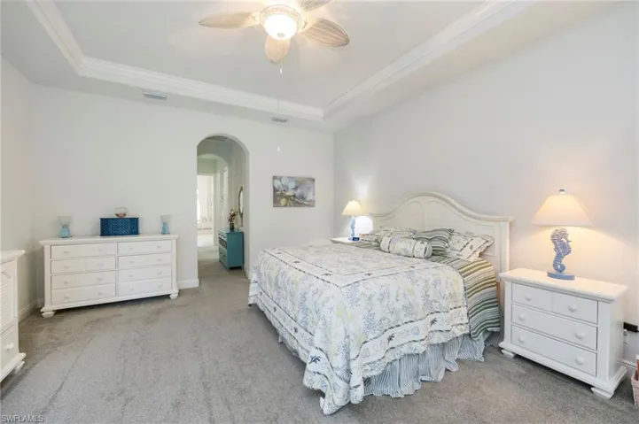 Bedroom with arched walkways, light carpet, a ceiling fan, a raised ceiling, and crown molding