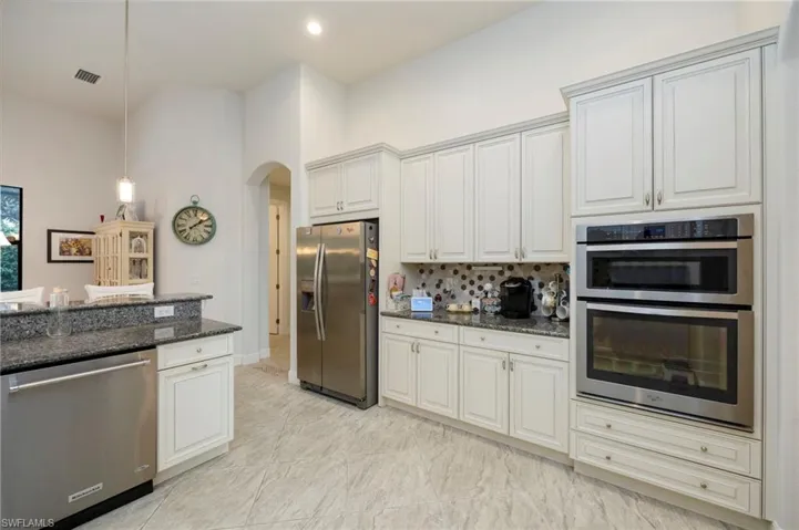 Kitchen with appliances with stainless steel finishes, arched walkways, dark stone countertops, hanging light fixtures, and white cabinets